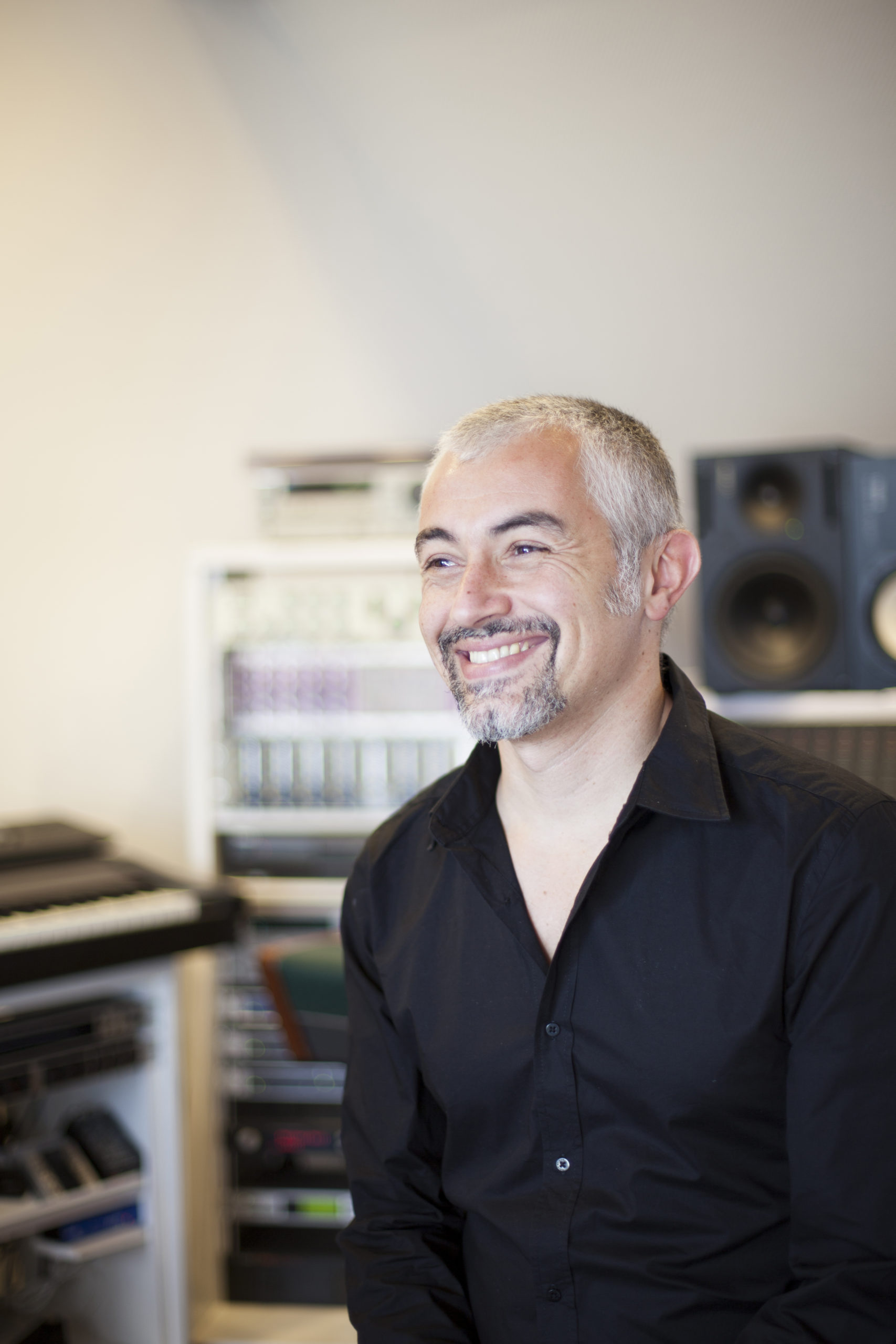 Bojan Vuletic steht in einem Studioraum, umgeben von Technik und lächelt jemanden an.