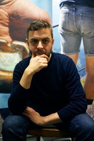 Christoph Westermeier sitzt vor einer groeßen, zweigeteilten Fotografie und schaut direkt in die Kamera